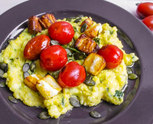 Zucchini Polenta Halloumi: Teller mit Cremepolenta darauf Halloumi Würfel und Cocktailtomaten