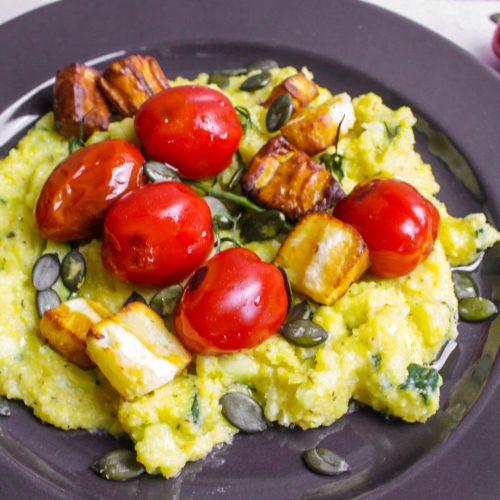 Zucchini Polenta Halloumi: Teller mit Cremepolenta darauf Halloumi Würfel und Cocktailtomaten