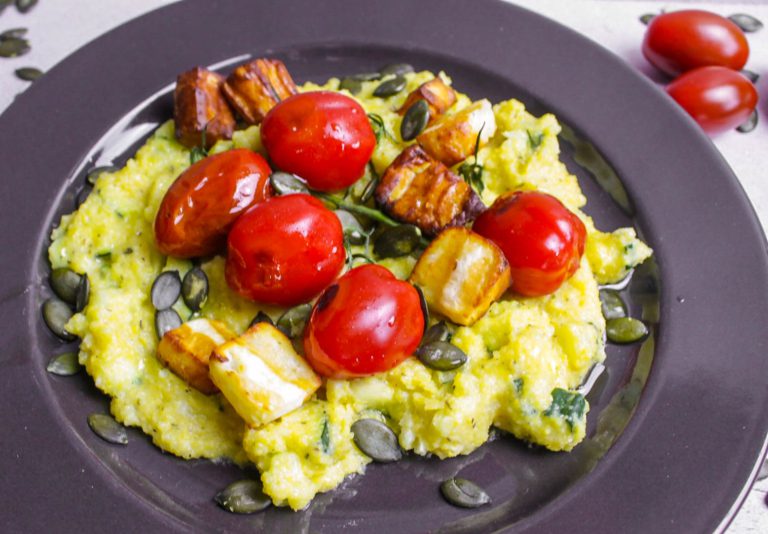 Zucchini Polenta Halloumi: Teller mit Cremepolenta darauf Halloumi Würfel und Cocktailtomaten