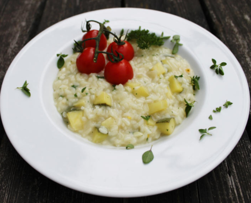 Zu sehen ist ein Teller schräg von oben fotografiert mit Zucchinirisotto und einer Rispe Cocktailtomaten