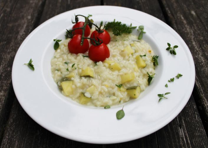 Zucchini-Risotto ohne Wein Zu sehen ist ein Teller schräg von oben fotografiert mit Zucchinirisotto und einer Rispe Cocktailtomaten